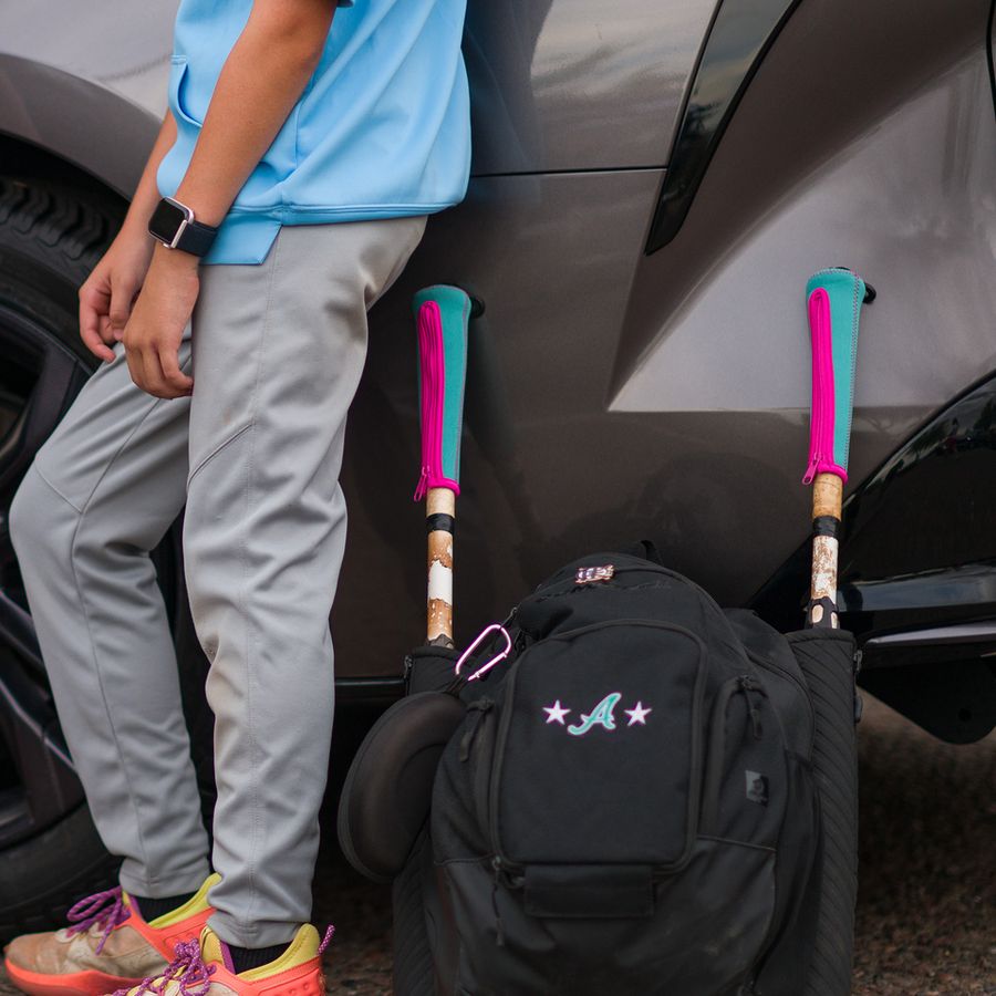 Player leaning on a car with covered bats in a bat bag